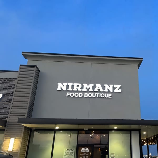 Exterior of Nirmanz Food Boutique with its illuminated sign against a clear blue sky.