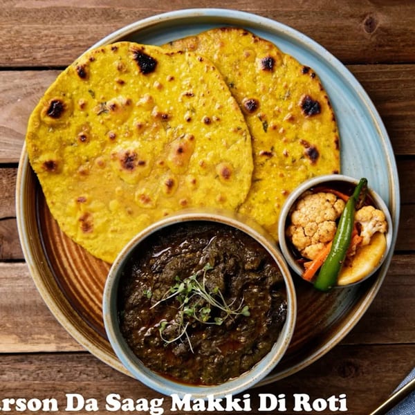 Nirmanz Food Boutique's Sarson Da Saag Makki Di Roti, a traditional Indian dish with flatbread, curry, and pickled vegetables.