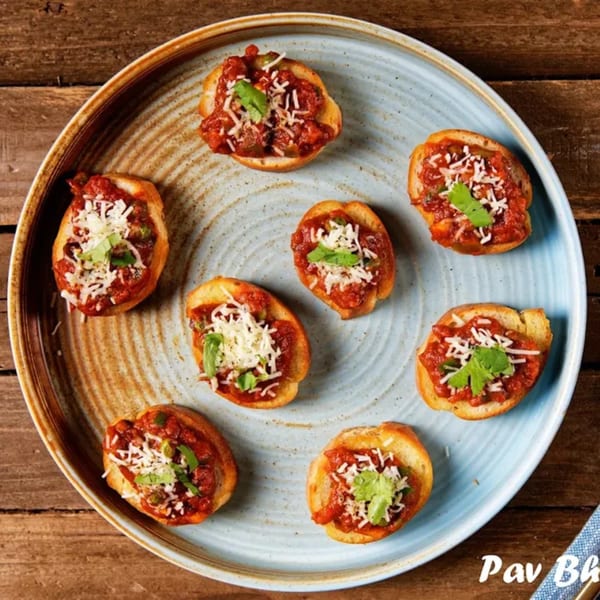 Seven Indian Pav Bhaji bruschettas, topped with red sauce, cheese, and cilantro, on a blue plate.