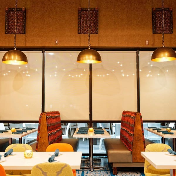 Nirmanz Food Boutique's dining area with patterned booths, white tables, and golden pendant lights.