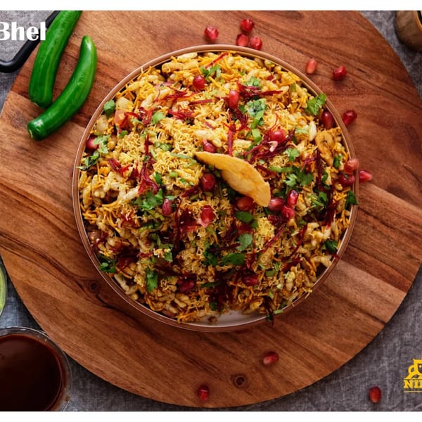 A vibrant bowl of Nirmanz Bhel Puri, garnished with pomegranate seeds and fresh cilantro, on a wooden board.