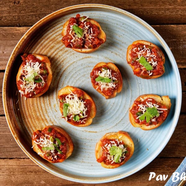Seven Pav Bhaji bruschettas, topped with cheese and cilantro, arranged on a blue plate.