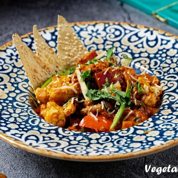 Nirmanz Food Boutique's Indian vegetable curry with cauliflower, peppers, and papadum in a patterned bowl.
