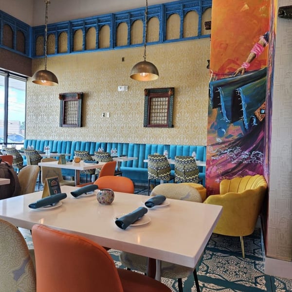 Vibrant Indian restaurant interior with blue banquettes, patterned chairs, and colorful wall art at Nirmanz Food Boutique.