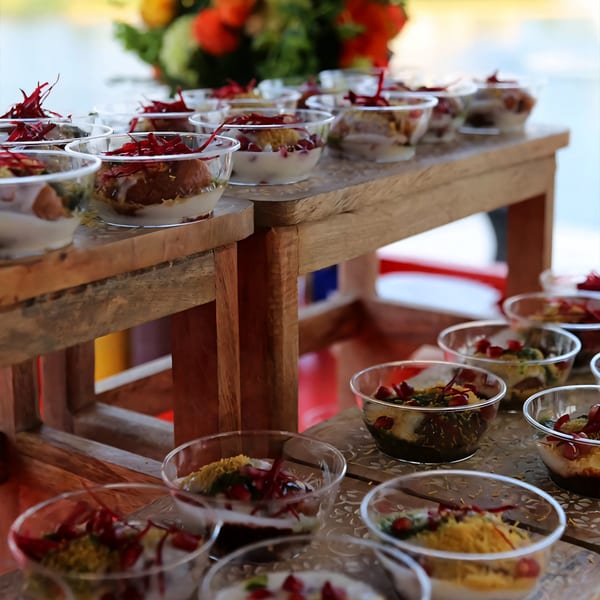Rows of Indian chaat desserts in clear bowls with red garnish on wooden stands.