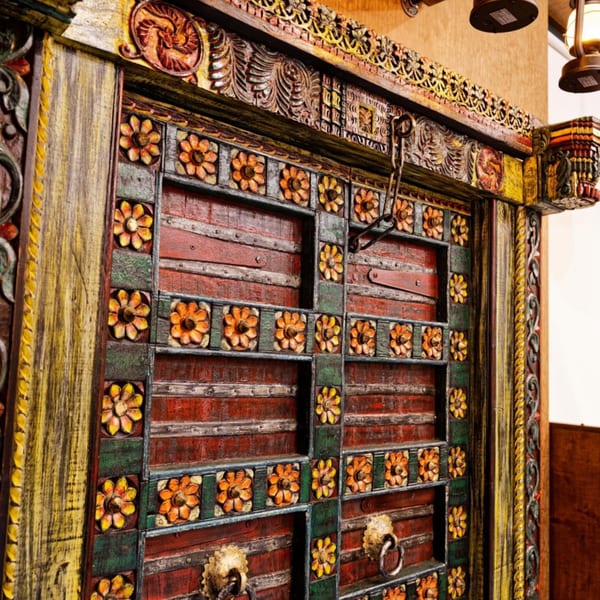 Intricately carved, colorful wooden door with floral patterns and metal accents, reflecting Indian decor.