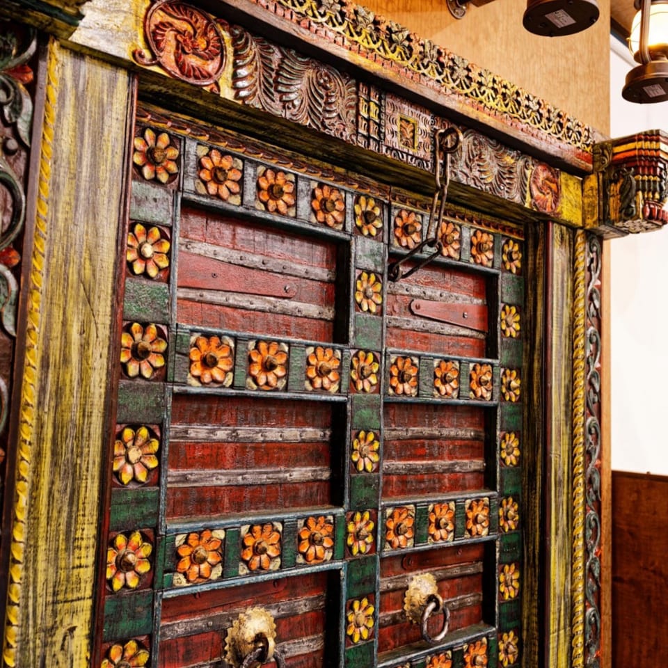Intricately carved, colorful wooden door with floral patterns and metal accents, reflecting Indian decor.