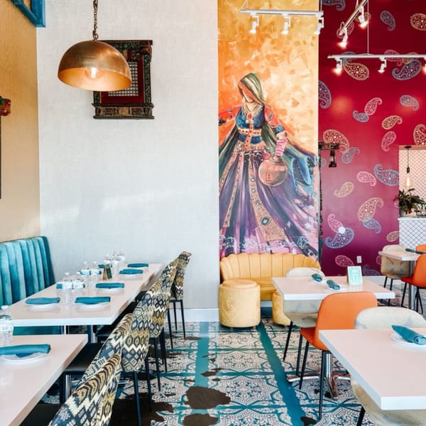 Vibrant Indian restaurant interior with colorful murals, patterned chairs, and set tables.